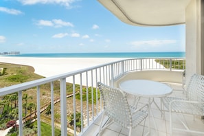Un balcon avec des balustrades en métal blanc, une table ronde et deux chaises en osier.