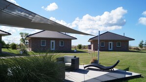 Two brick houses with tiled roofs, a patio with a lounge chair, and a large umbrella providing shade. - Strandleben Fehmarn - Ferienwohnung Ost (Fehmarn)