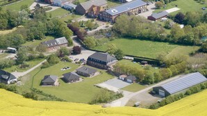 An aerial view of a residential area with houses, a large building with solar panels, and a field of yellow flowers. - Strandleben Fehmarn - Ferienwohnung Ost (Fehmarn)