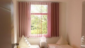A room with two single beds, a window with pink curtains, and a bedside table with a lamp. - Strandleben Fehmarn - Ferienwohnung Ost (Fehmarn)