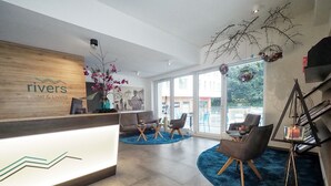 Zona de recepción de hotel con diseño moderno, que incluye un mostrador de recepción, un área de estar con sofás y sillones, y ventanas amplias con vistas al exterior.