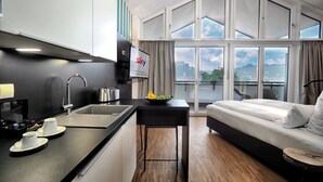 Habitación de hotel moderna con cocina, una mesa de comedor, sofá y ventanas amplias con vista a la ciudad.