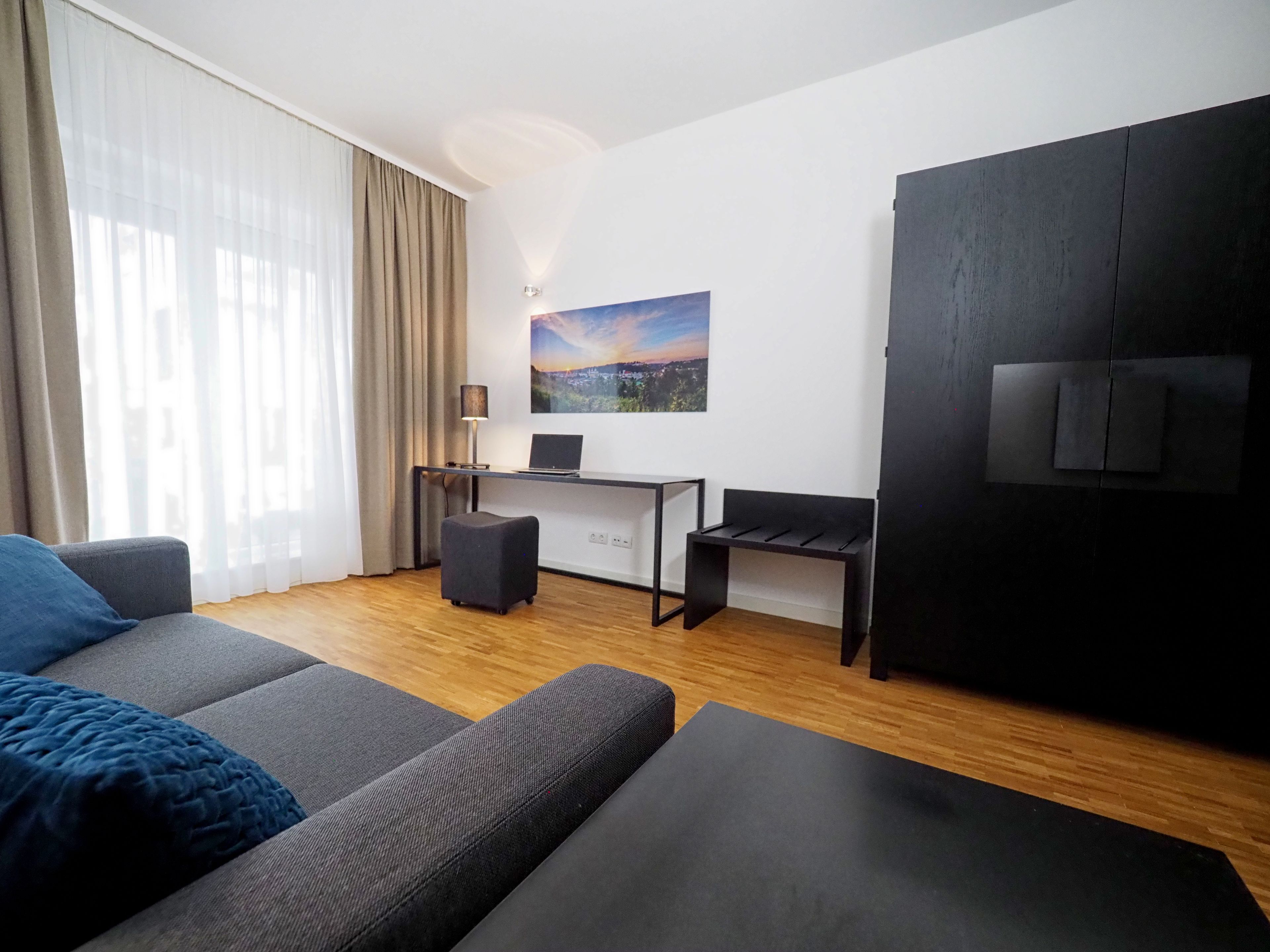 A modern living room with a sofa, a desk with a laptop, a small table, and a TV.