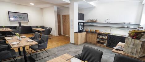 Un comedor de hotel moderno con mesas de madera, sillas negras y un mostrador de bufé con diversos alimentos.