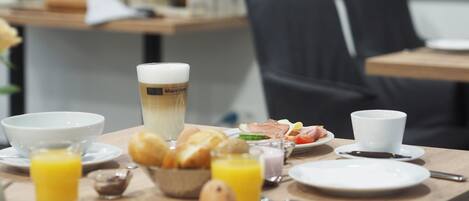 A breakfast table with a cup of coffee, croissants, a plate of ham and cheese, and a glass of orange juice.