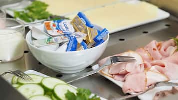 A buffet with various food items including sliced cucumbers, tomatoes, and ham, along with containers of yogurt and butter.