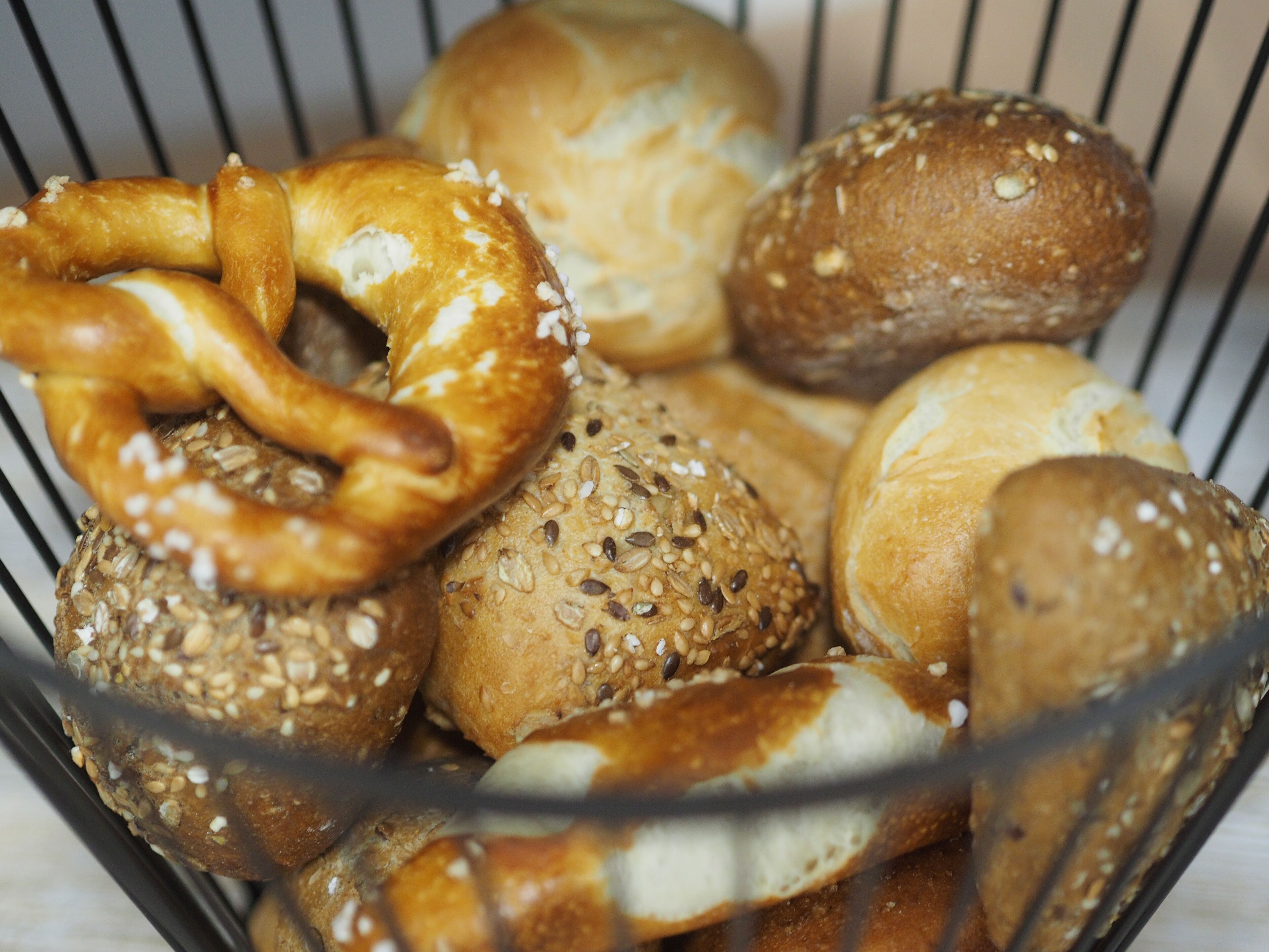 A basket containing various types of bread, including pretzels and rolls with seeds.