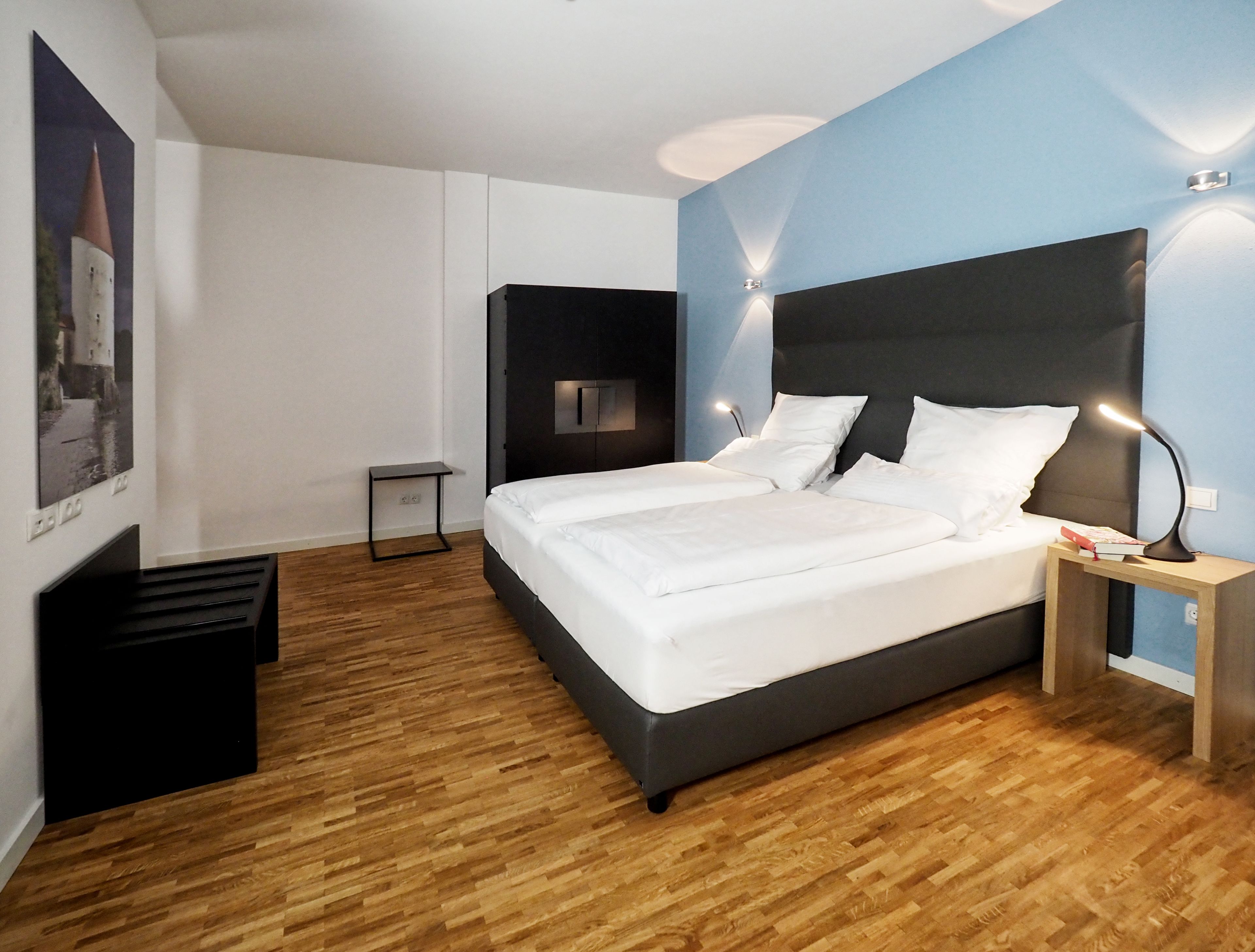 Un dormitorio moderno con una cama grande, una mesita de noche pequeña, un estante en la pared y un cartel.