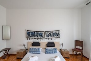 A bedroom with a bed, two nightstands, a chair, and two wall-mounted tapestry artworks.