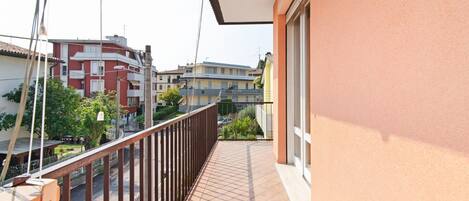 A balcony with a metal railing, a view of neighboring buildings, and a clear sky.