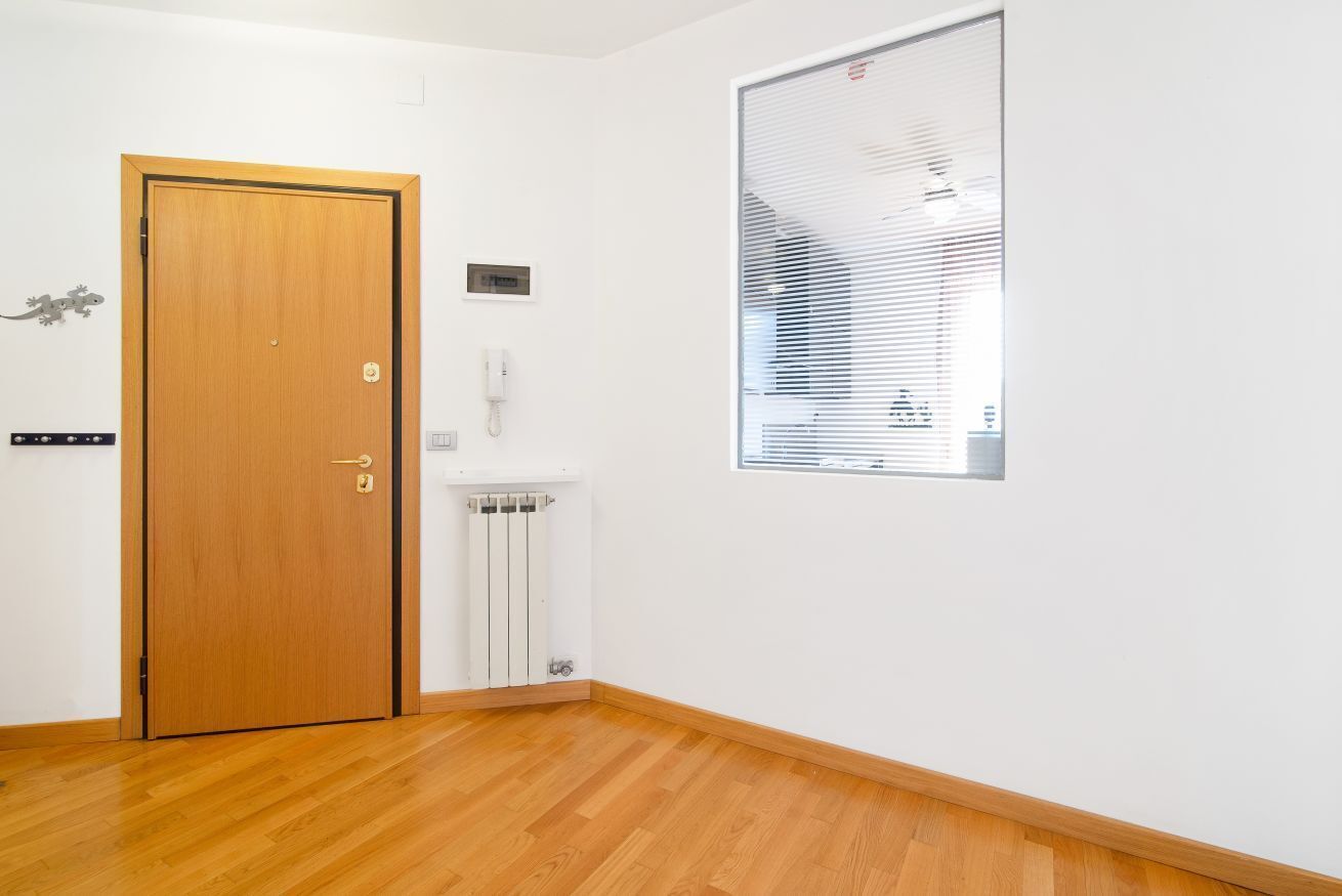 Une pièce avec une porte en bois, un radiateur, un téléphone et une fenêtre avec des stores.