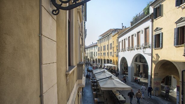 Une rue étroite avec des terrasses, des bâtiments dotés d’arcades et un chemin pavé.