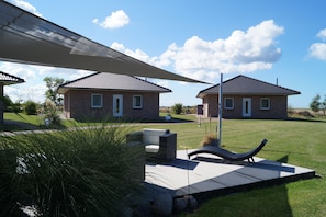 Two brick houses with tiled roofs, a patio with a lounge chair, and a large umbrella providing shade. - Strandleben Fehmarn - Ferienwohnung Süd (Fehmarn)