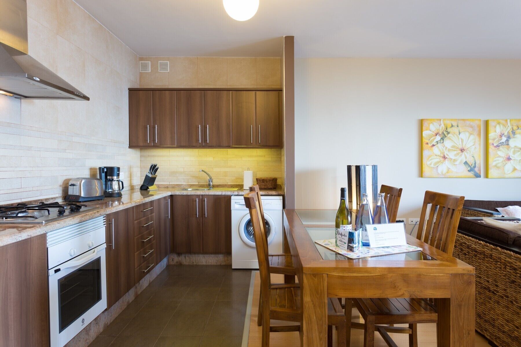 Une cuisine compacte avec des meubles en bois, un four encastré, un lave-linge et un coin repas comprenant une table et des chaises en bois.