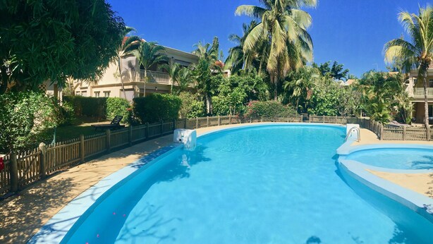 Une piscine dotée d’une terrasse en bois et d’une clôture, entourée d’une végétation luxuriante et de palmiers.