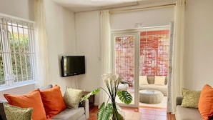 Un salon avec un canapé gris, des coussins orange, une table basse en bois et un téléviseur fixé au mur.