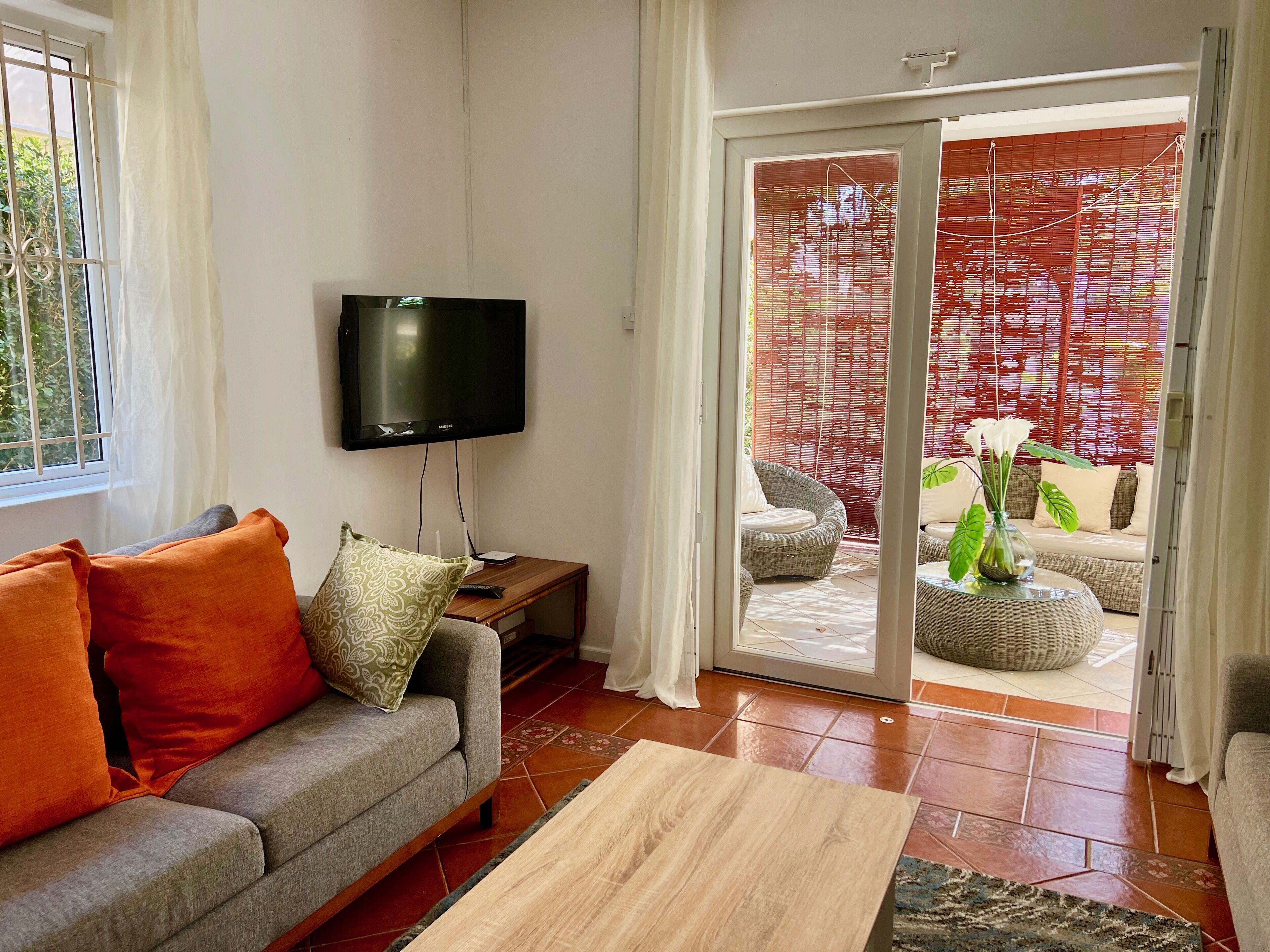 A living room with a sofa, a flat-screen TV, a wooden coffee table, and a sliding glass door leading to an outdoor seating area.