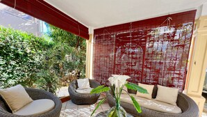 Une terrasse ensoleillée avec des meubles en osier, un vase en verre rempli de fleurs et un paravent en bambou rouge.