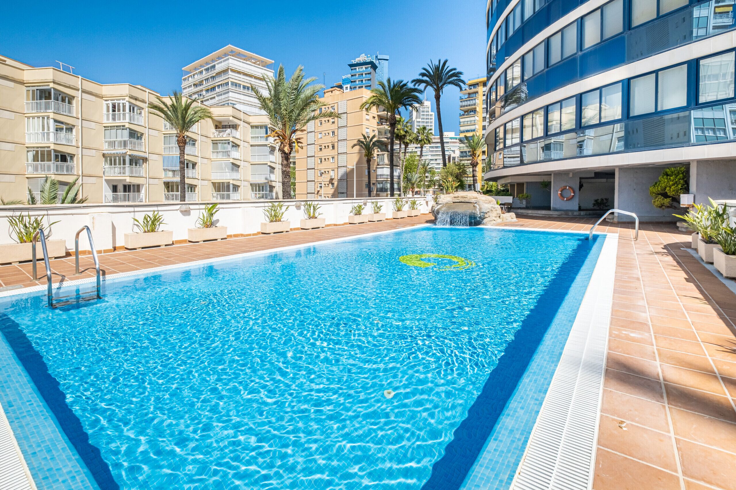 A rectangular swimming pool with clear blue water, surrounded by a tiled deck.