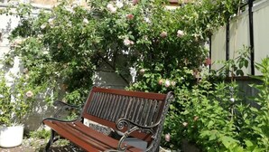 A wooden bench with a metal frame, positioned in front of a flowering bush with pink blossoms. - Pension Carmen (Bad Hoenningen)