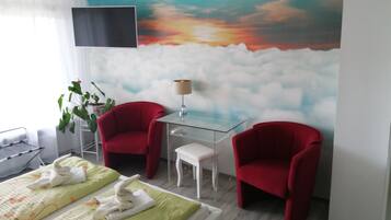 Una habitación de hotel con una cama, dos sillones rojos, una mesita con una lámpara y un gran mural de un atardecer en la pared.