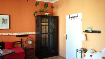 Una habitación con pared naranja, un mueble negro, una cama con ropa de cama floral, una silla roja y una mesita.