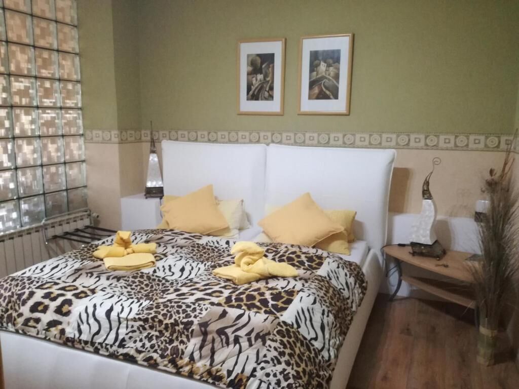 Una habitación de hotel con una cama, dos cuadros en la pared, una mesita de noche con lámpara y una ventana con persianas.