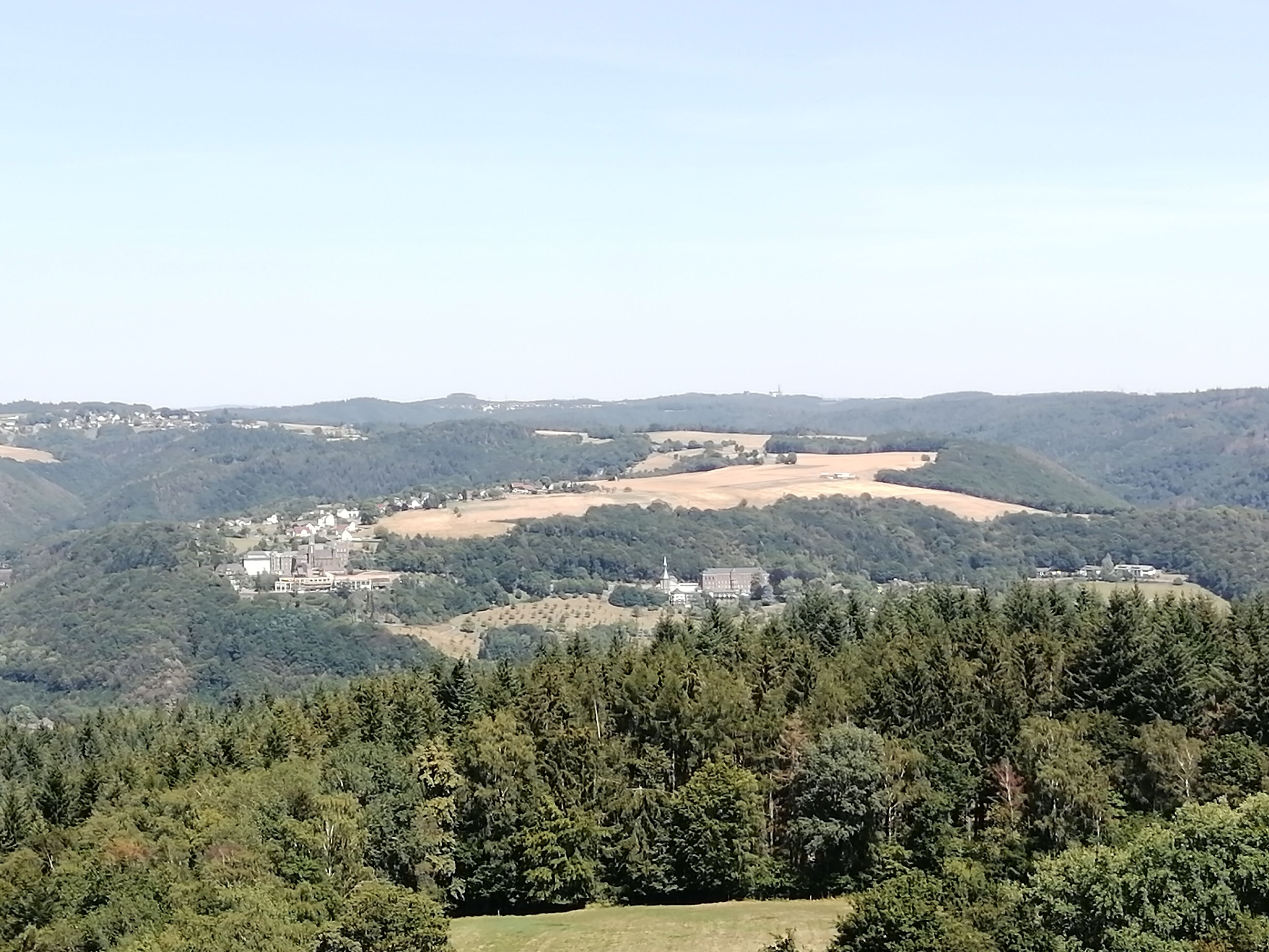 Una vista panorámica de un paisaje rural con un conjunto de edificios rodeado de densos bosques y ondulantes colinas.