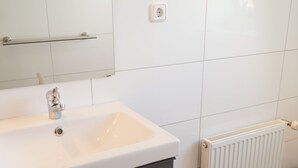 Um banheiro com pia branca, espelho, porta-toalhas e radiador.