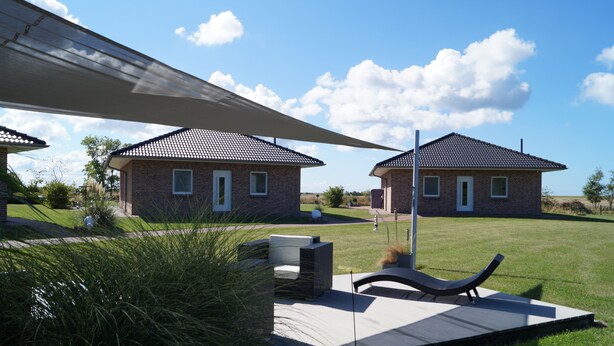 Duas casas de tijolo com telhados de cerâmica, um pátio com espreguiçadeira e um grande guarda-sol para proteção do sol.