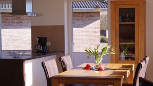 A modern kitchen with a dining area, featuring a wooden table and chairs, a coffee maker, and a view of the outside. - Strandleben Fehmarn - Ferienhaus 1 (Fehmarn)