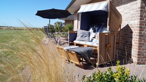 A patio area with wicker furniture, a large umbrella, and a brick building. - Strandleben Fehmarn - Ferienhaus 1 (Fehmarn)