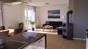 A modern kitchen with a built-in stove, dining area with chairs and a table, a sofa, and a potted plant. - Strandleben Fehmarn - Ferienhaus 1 (Fehmarn)
