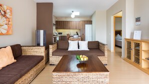 Una sala de estar con muebles de mimbre, una mesa de centro de madera con fruta y vista a la cocina.