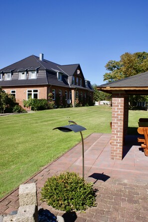 Een bakstenen huis met een verzorgd gazon, een terras en een kleine tuin.