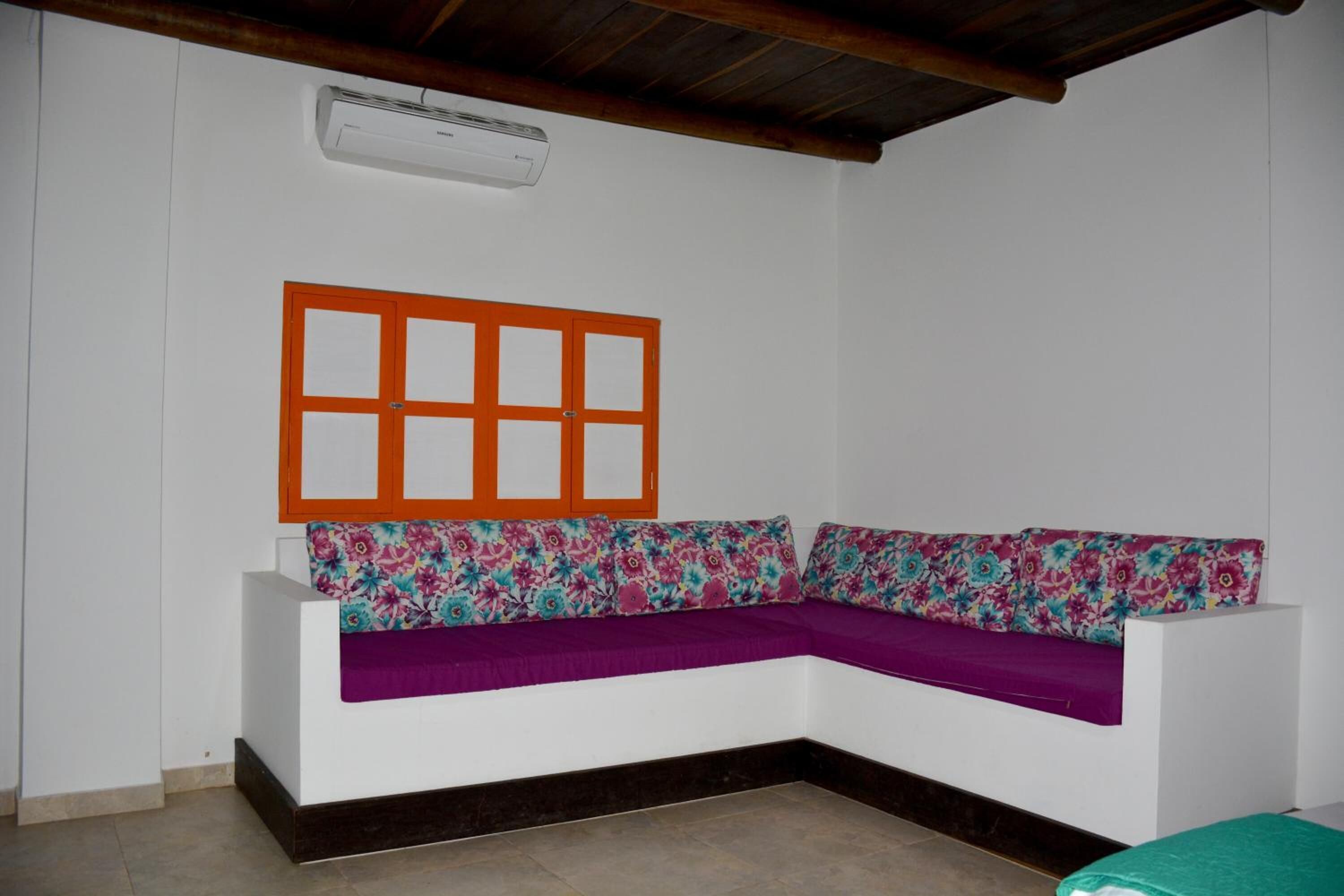 Ein Eckzimmer mit einem weißen Sofa, violetten Kissen und einem Fenster mit Holzrahmen.