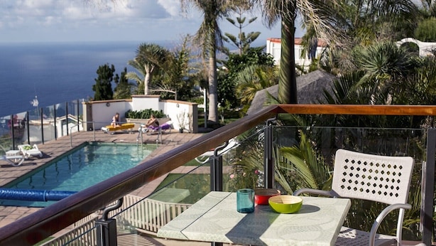 Area piscina con vista sul mare, un tavolo con una ciotola e un bicchiere, e poltrone prendisole.