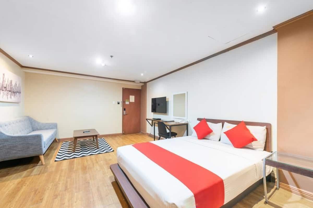 A hotel room with a bed, a desk, a chair, a sofa, and a television.