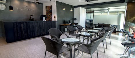 A hotel reception area with a dark reception desk, multiple seating arrangements, and ceiling fans.