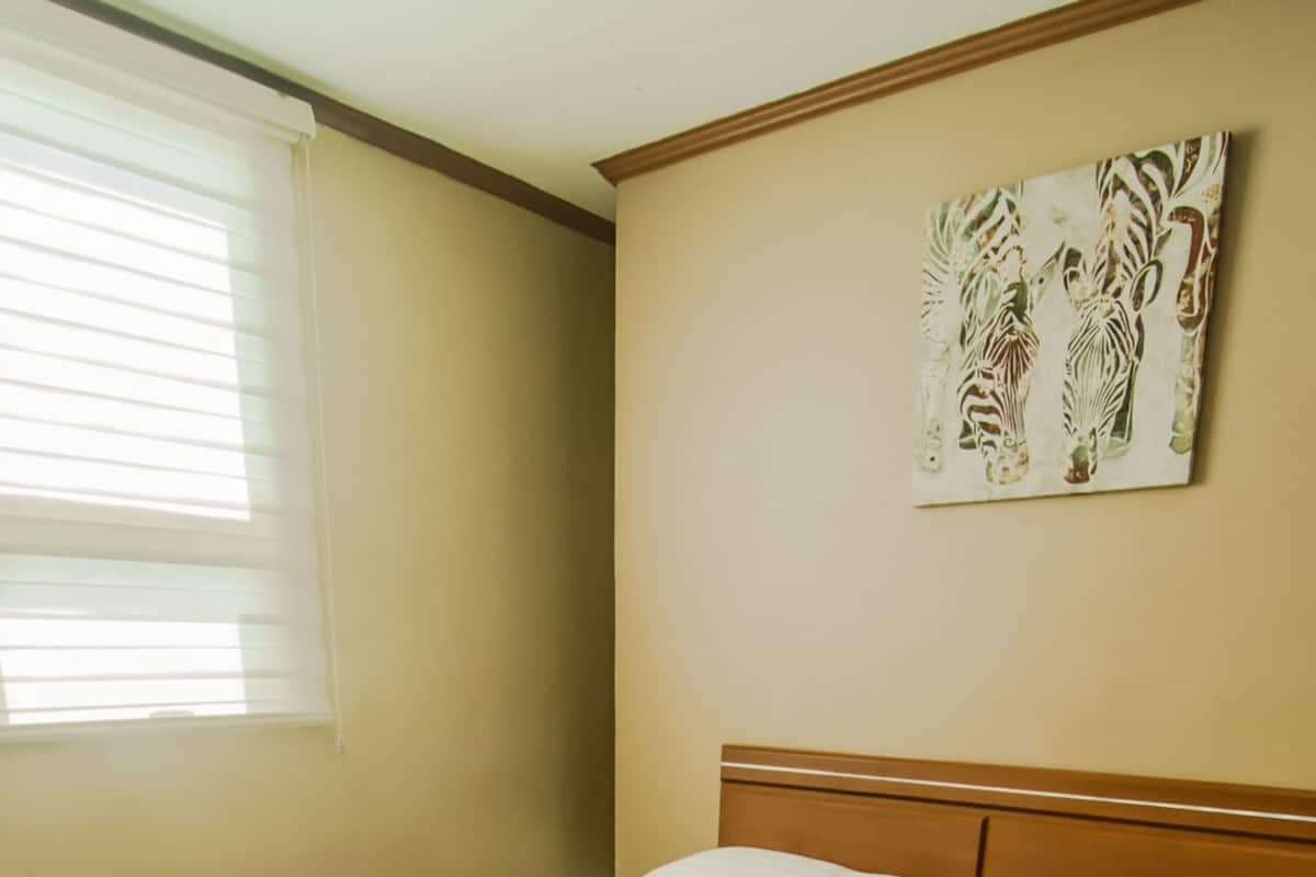 A neatly made bed with a patterned bedspread, a wooden headboard, and a wall-mounted zebra artwork.