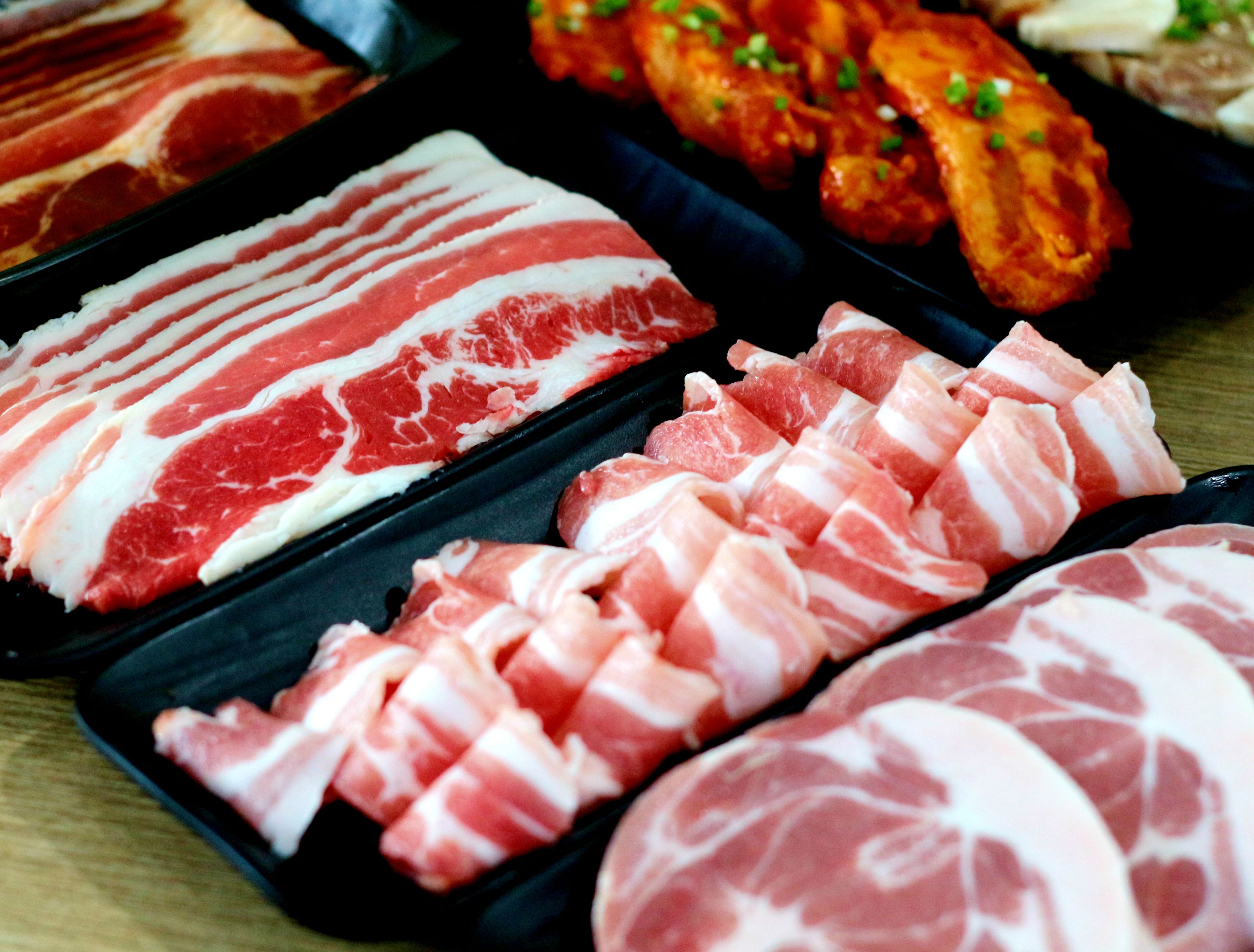 A variety of raw meats, including different cuts of pork and beef, displayed on trays.