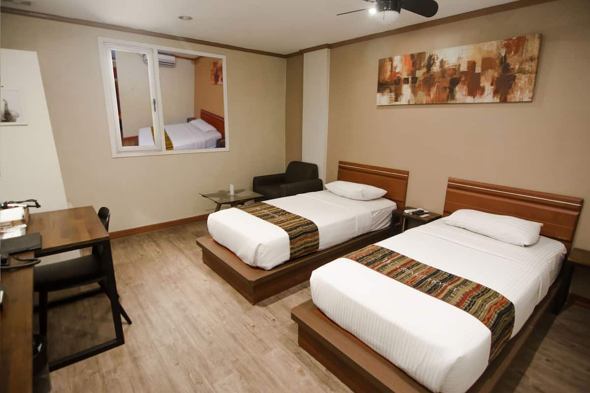 A hotel room with two beds, a desk, a chair, a small table, and a ceiling fan.