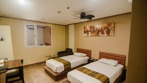 A hotel room with two beds, a desk, a chair, a ceiling fan, and a painting on the wall. - DG Grami Hotel (Parañaque)