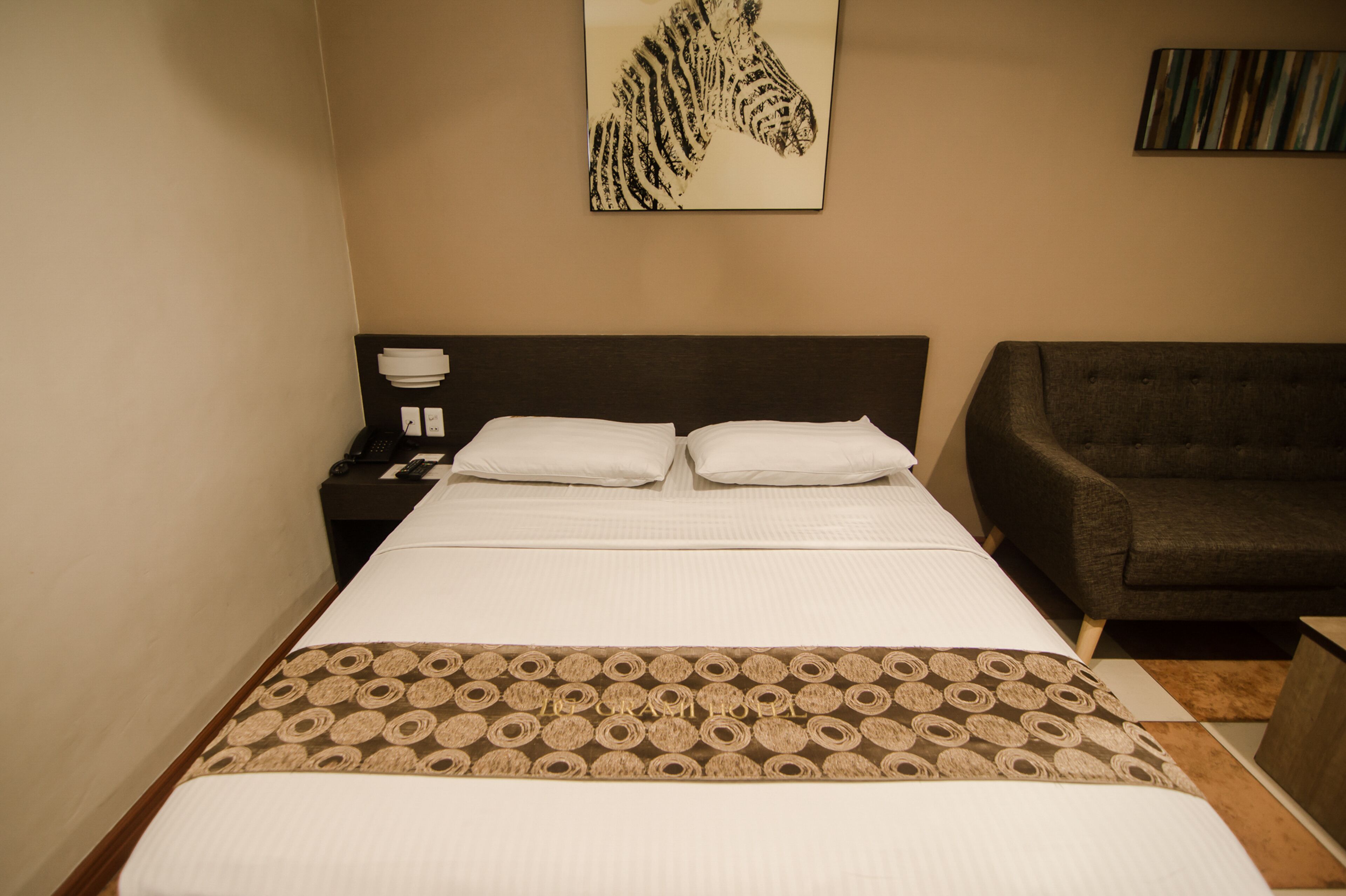 A hotel room with a bed, a nightstand, a lamp, a sofa, and a zebra artwork on the wall.