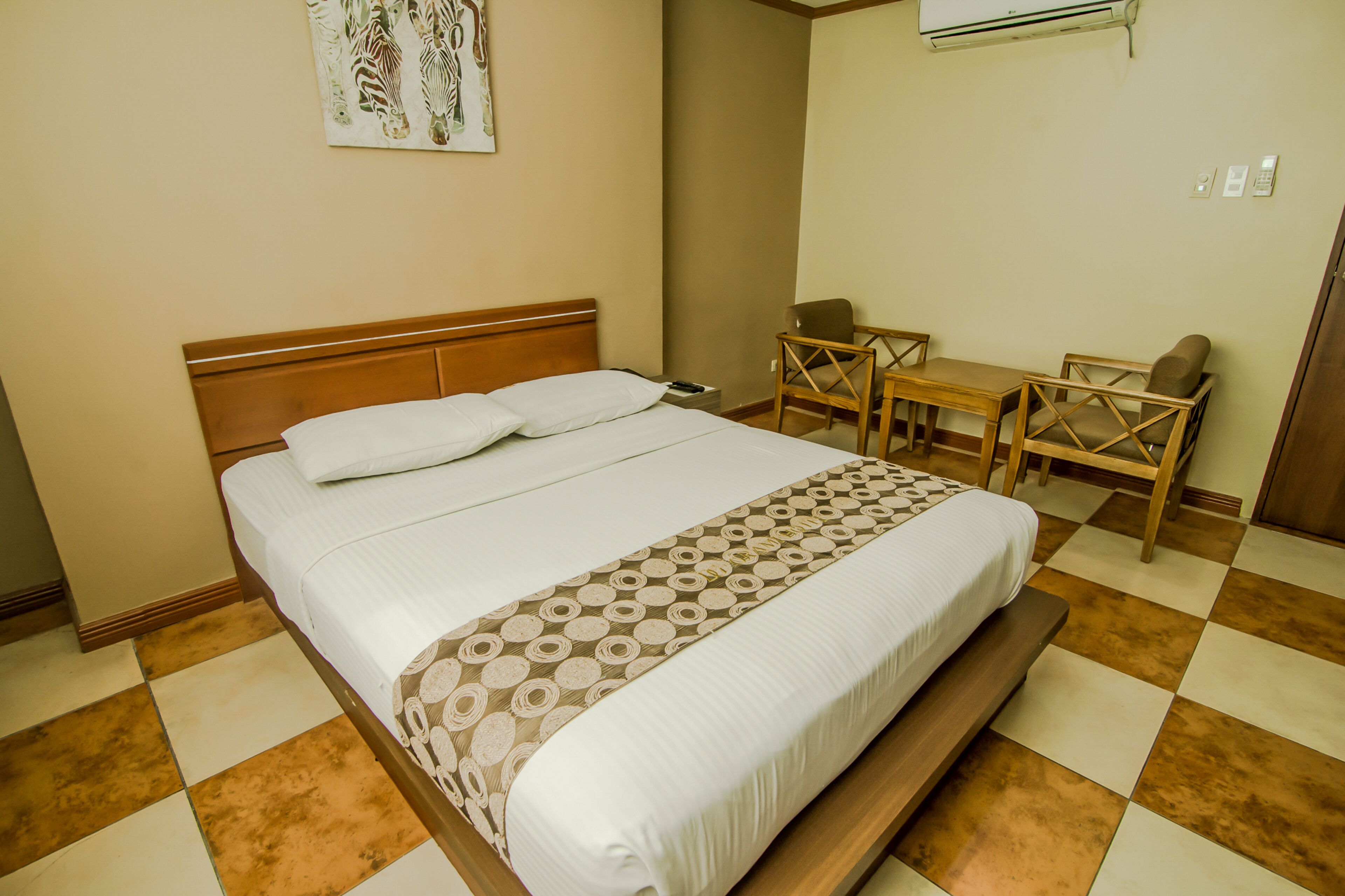 A neatly made bed with a patterned bedspread, a wooden headboard, and a bedside table with a lamp.