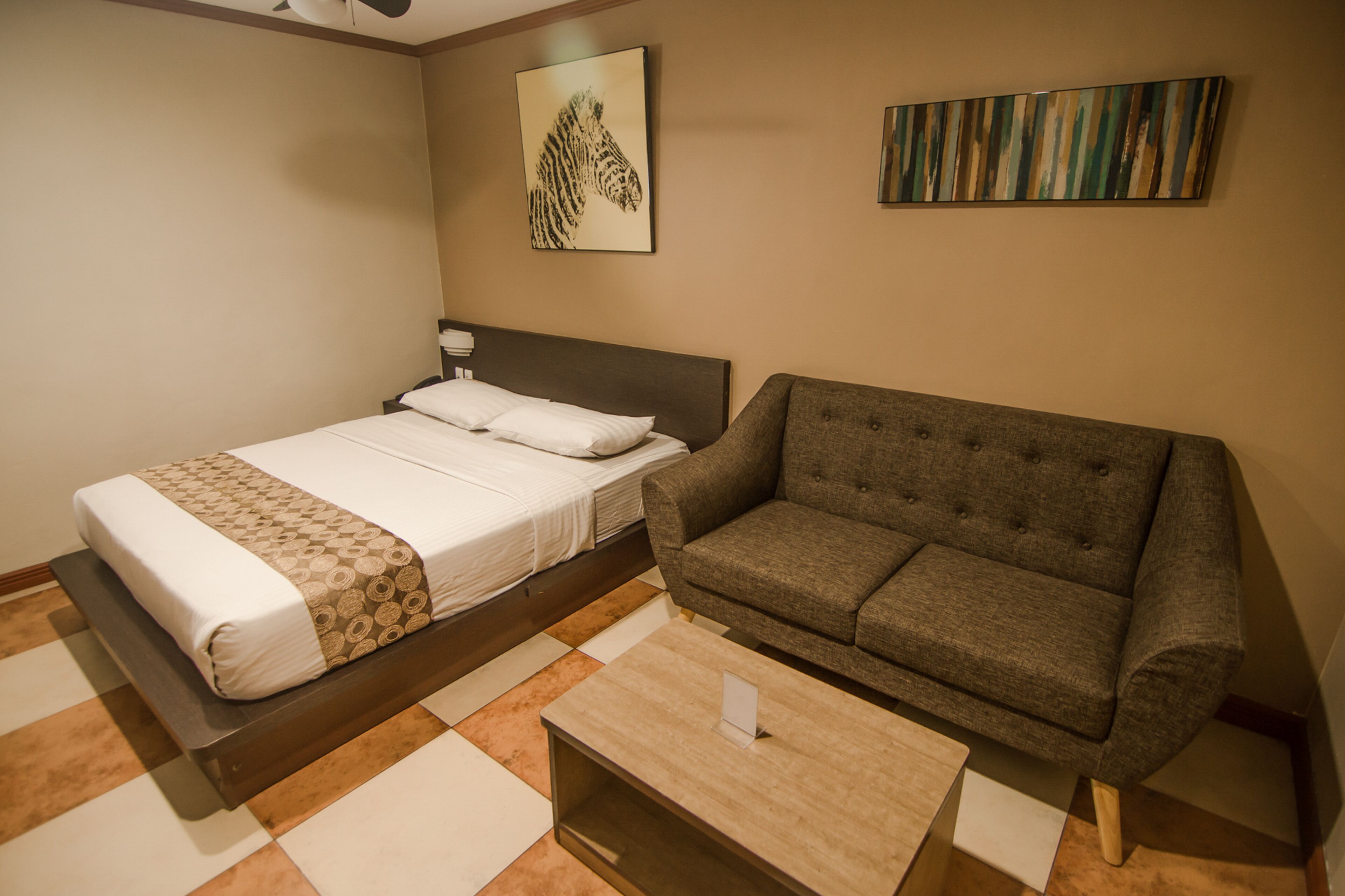 A hotel room with a bed, a sofa, a coffee table, and artwork on the walls.