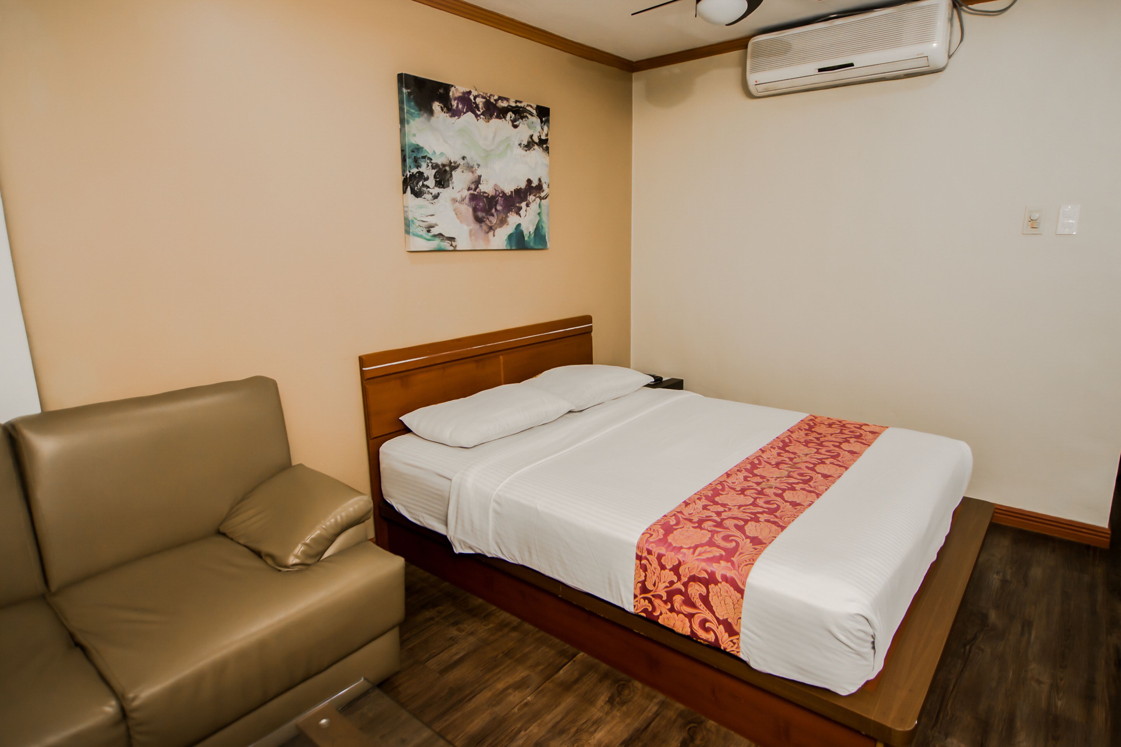 A bedroom with a bed, a wooden headboard, a beige sofa, and a ceiling fan.