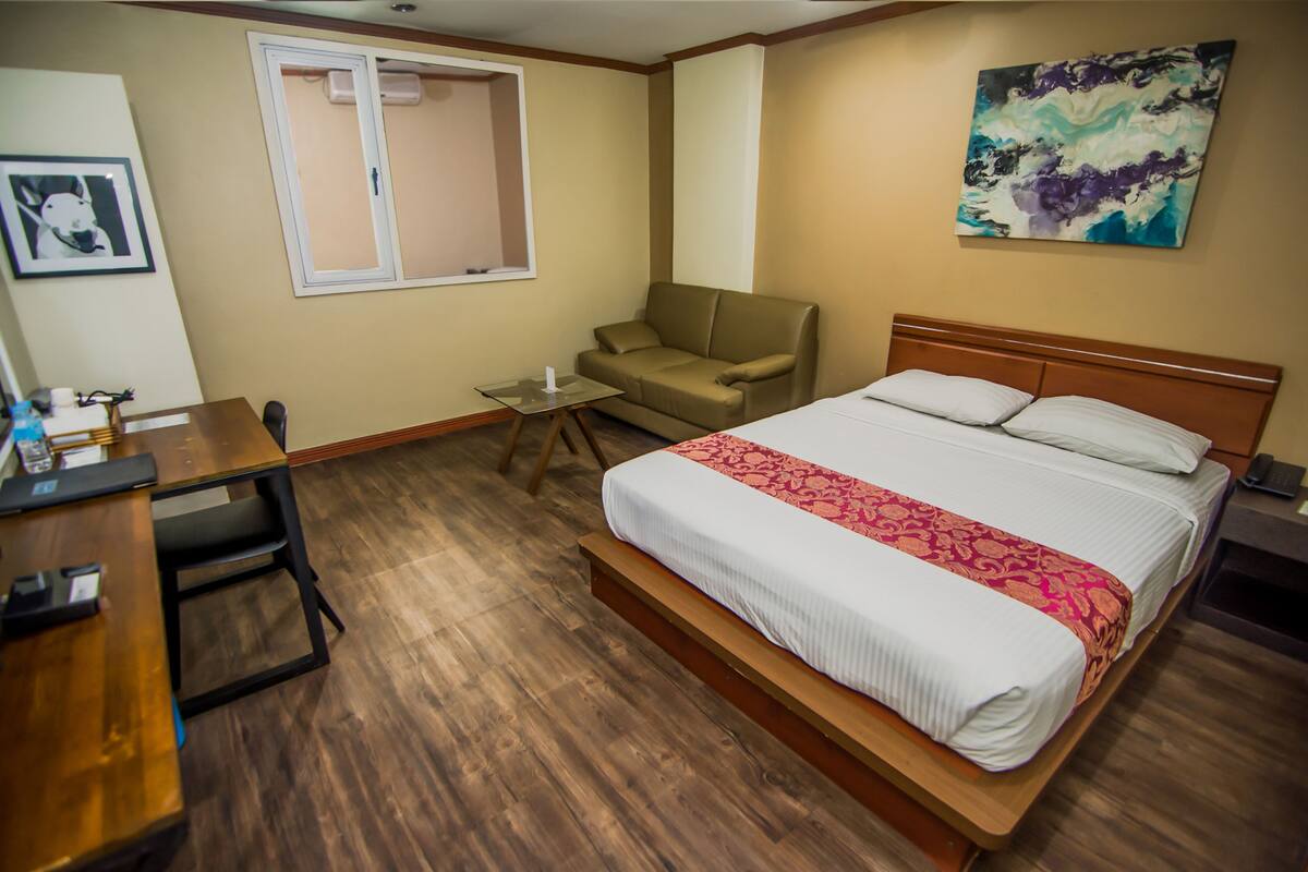 A hotel room with a bed, a desk, a chair, a small table, and a window.