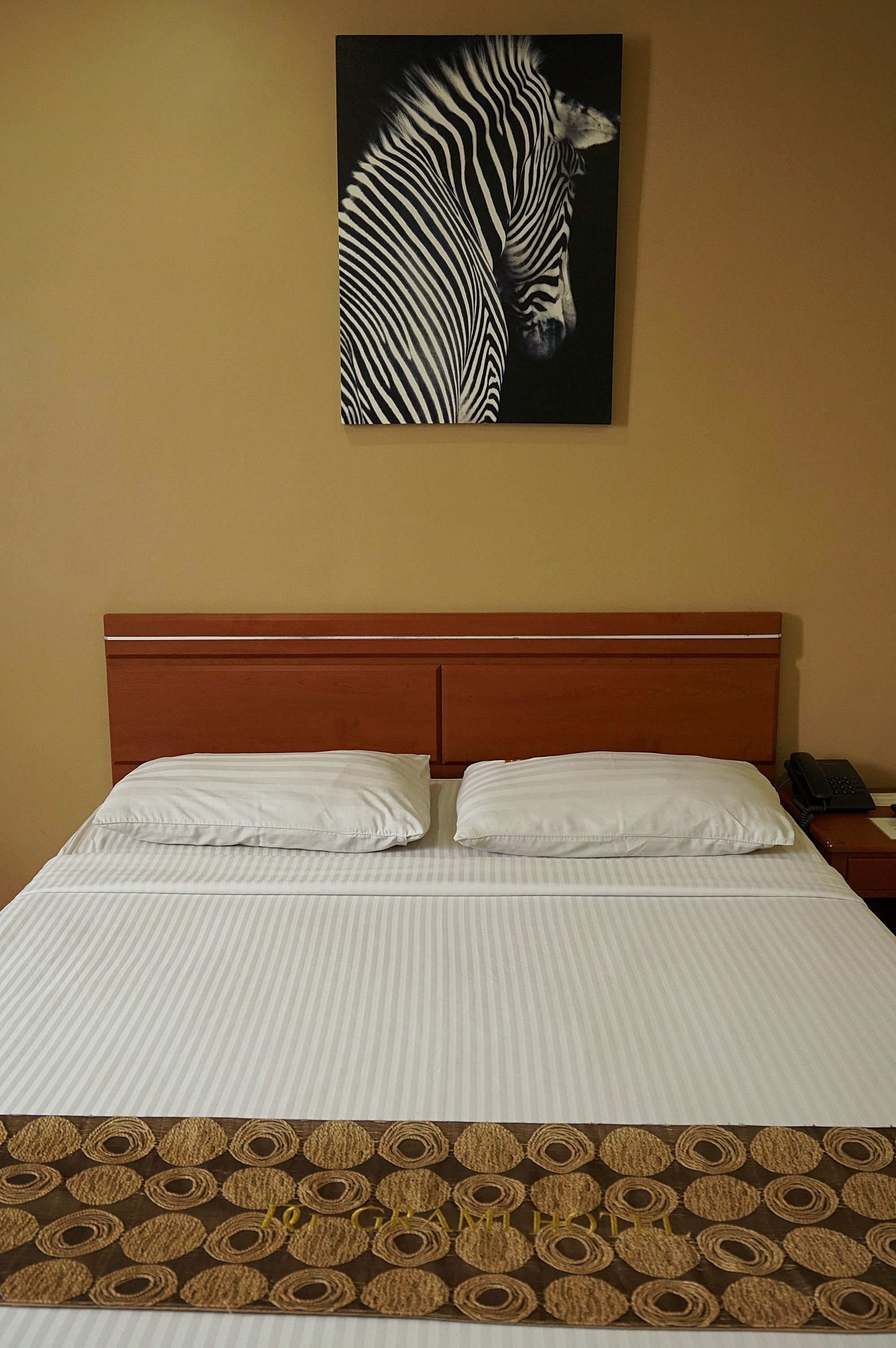 A neatly made bed with a striped bedspread and two pillows, a wooden headboard, and a wall-mounted zebra artwork.