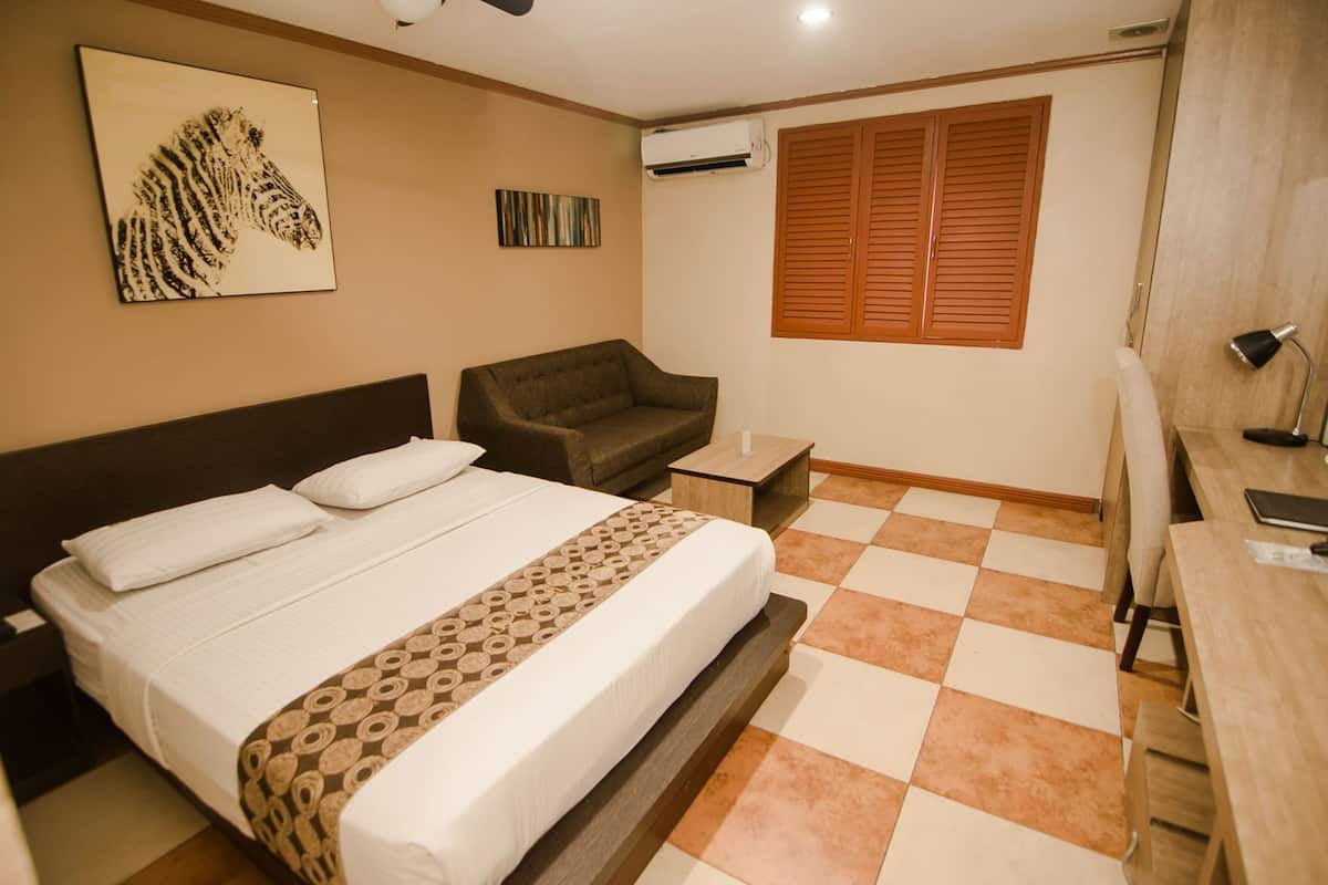 A hotel room with a bed, a sofa, a desk, and a window with wooden shutters.